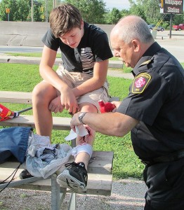 Declan Cook of Tilbury gets some fake blood poured into his equally fake leg wound at a mock accident July 10 at Percy Park in Chatham by Assistant Fire Chief Ric Scharf. Cook took part in a week-long summer camp that exposes local high school students to various health-care and emergency services professions. The 10 local kids played victims at the mock accident, where a car was to have run into the bleachers at a ball field, as well as members of the emergency services called in to aid the injured.