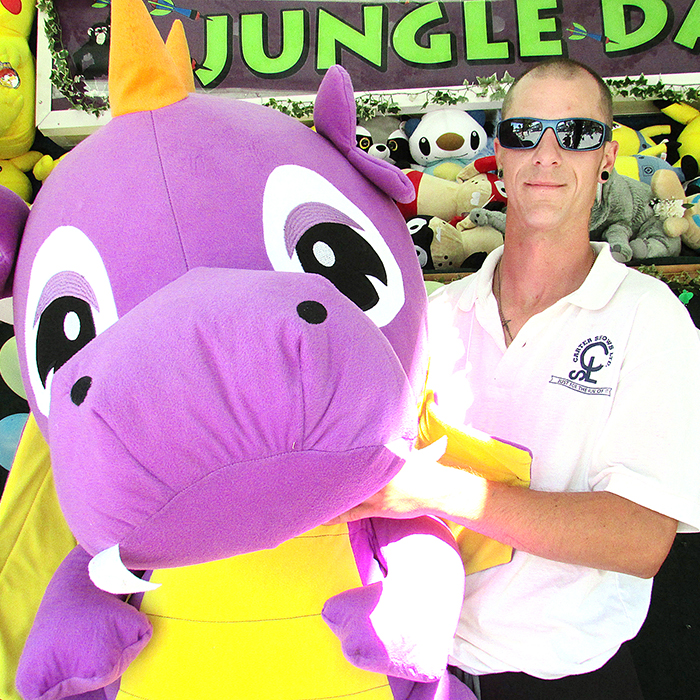 James Sharp with Carter Shows hawks his wares at the Jungle Darts booth at Blenheim CherryFest Thursday. The purple dinosaur is the biggest prize for popping balloons with darts.