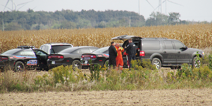 Chatham-Kent police gather outside a corn field east of the airport Friday.
