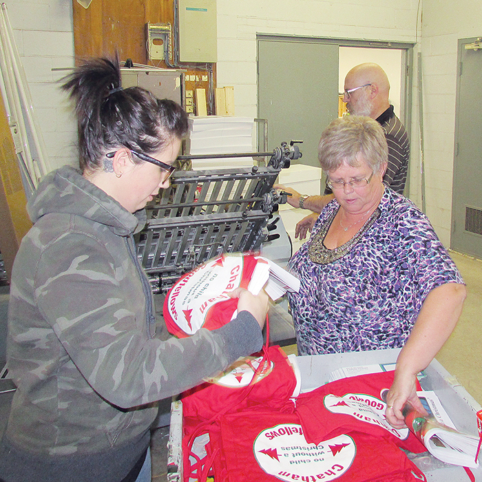 Chamberlain employees, from left, Brianna Broadwood, Sandie Alward and Andy Van Zelst load Goodfellows papers as they come off the press.
