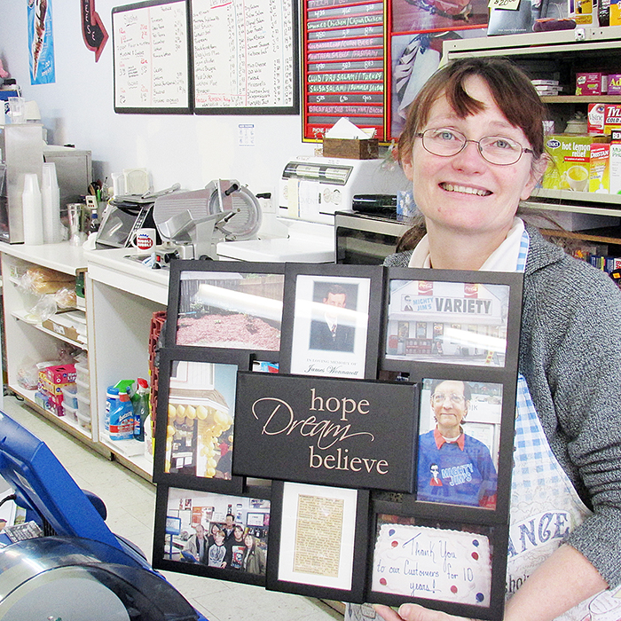 Joannie Wannacott holds a photo display featuring her husband Jim as she stands behind the counter at Mighty Jim’s Variety on Grand Avenue.