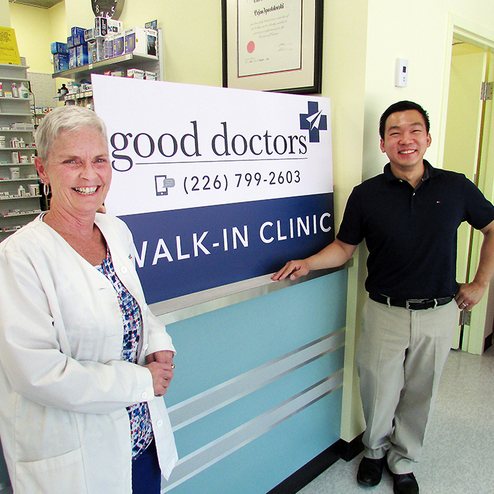 Patti Miller, staff pharmacist at Chatham Centre Pharmacy, left, and Lee Liao, director of Good Doctors Walk-In Clinics, showcase the sign for the new clinic that opens this week inside the pharmacy, which is located in the Downtown Chatham Centre.