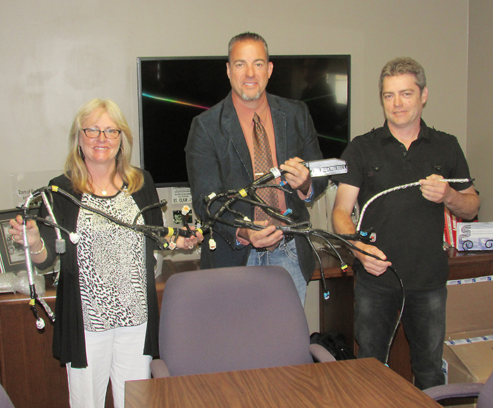 Jody Pilon, Charlie Hess and Randy Hess hold one of the automotive wiring harnesses designed by St. Clair Technologies of Wallaceburg. The firm recently celebrated 65 years in business.