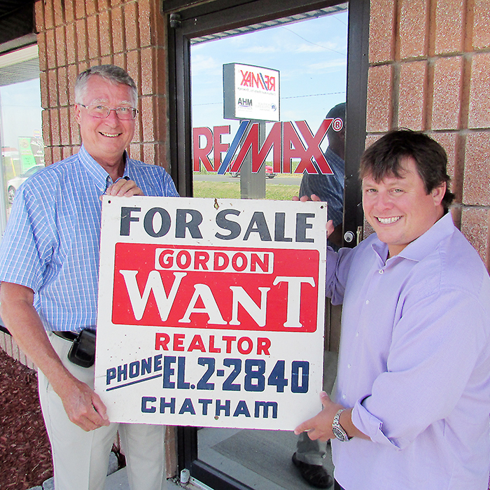 Darcy Want, left, and Rocky Gaudrault hold up a sales sign of Darcy’s father, Gord Want, who opened his real estate business in 1951. Darcy is now celebrating a half century following in his father’s footsteps, selling real estate. As for the phone number on the sign, EL-2-2840, it’s still the number at Gaudrault’s Re/Max office today – 519-352-2840.
