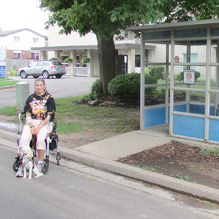 Patricia Wright sits on the road in her walker waiting for a bus on McFarlane Avenue because the bus shelter isn’t accessible.