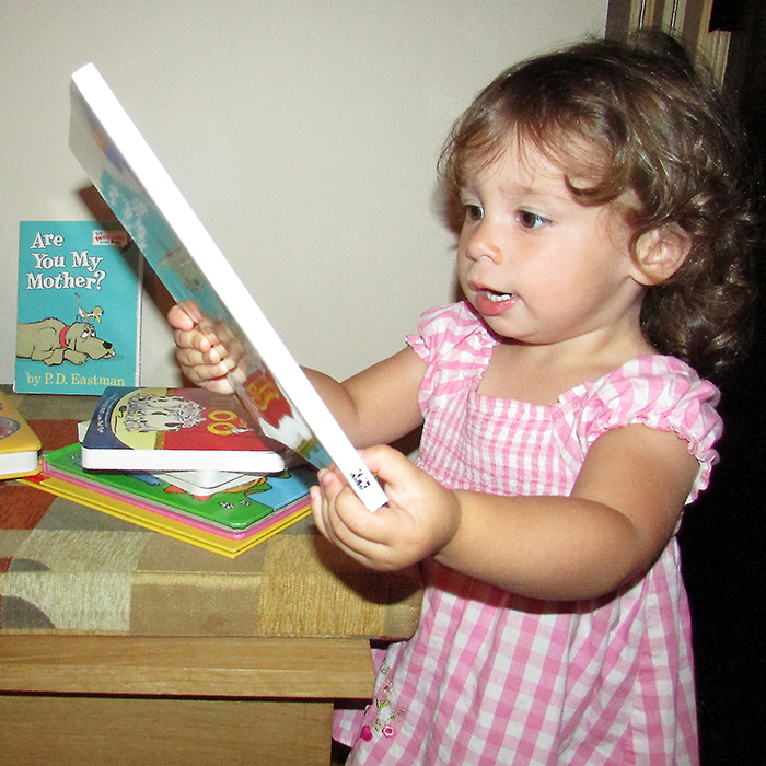 Children's books are stacked in the home of IMAGINATIONink's Patricia Weaver Blonde, whose granddaughter Jamie Lynn, pictured, enjoys looking at. The books are collected to go into the Christmas hampers of organizations that pack Christmas gift boxes.