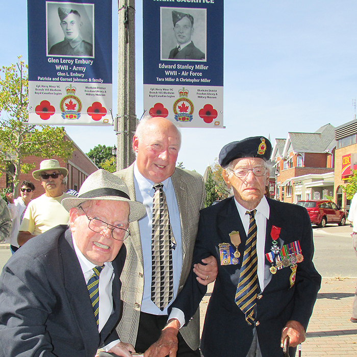 Second World War veterans Ed Miller, left and Glen Embury, right, stand below the banners in their honour outside the Br. 185 Blenheim Legion with the chair of the Honour Their Sacrifice committee, Doug Johnston, Sunday at an unveiling ceremony.