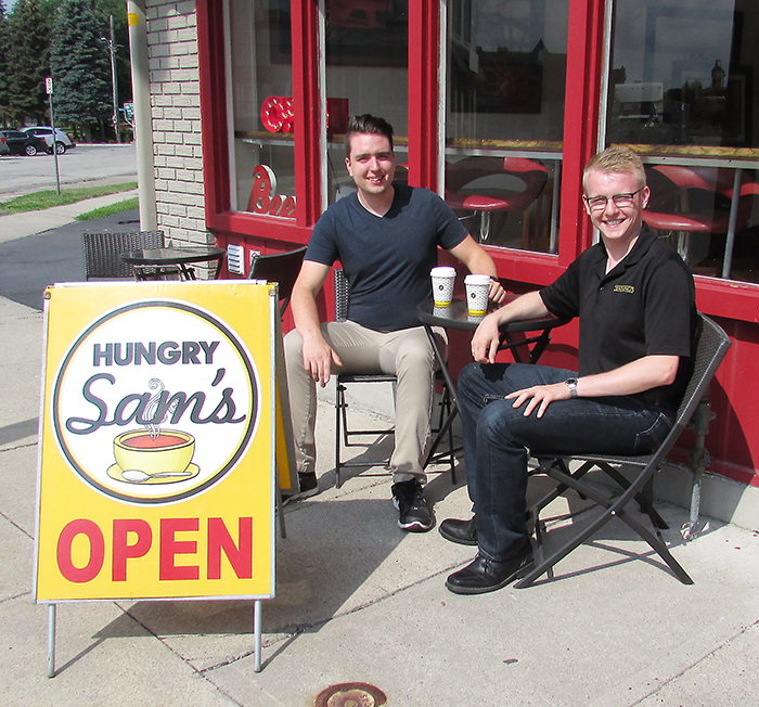 Sam Butler of Hungry Sam’s/Sam’s Percolator, left, and Jacob Rowe of Dennings of Chatham Funeral Home enjoy a coffee outside Butler’s restaurant on Thames Street. Rowe, in a random act of kindness, posted to social media an offer by the funeral home to purchase coffee for the first 100 people to stop by Hungry Sam’s on Aug. 2.