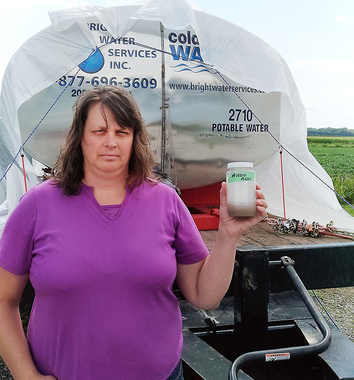 Jessica Brooks showcases the murky water now coming out of her taps at her home on Brook Line, north of Chatham. Behind her is a water tank Pattern Energy dropped off at her home.